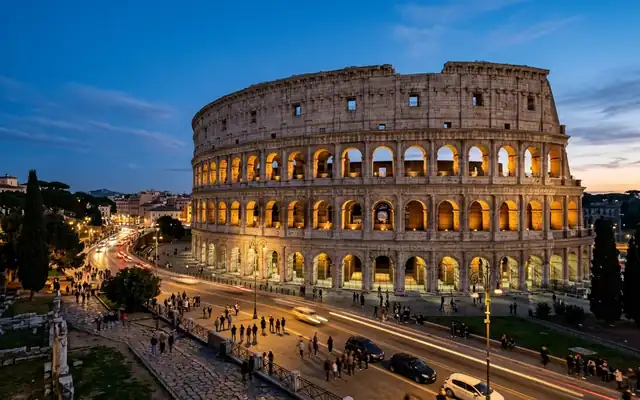 The Colosseum in Rome, Italy at dusk, its arched travertine tiers lit from within above the street below