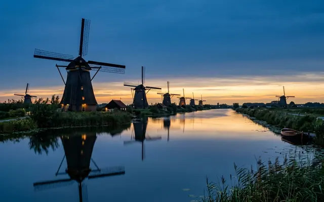 The Kinderdijk windmills in the Netherlands at dusk, their four-sailed silhouettes lining a calm canal and mirrored in the water