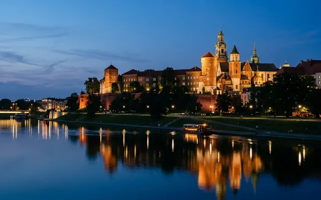 Wawel Royal Castle and its cathedral lit above the Vistula River in Krakow at dusk, reflected in the water