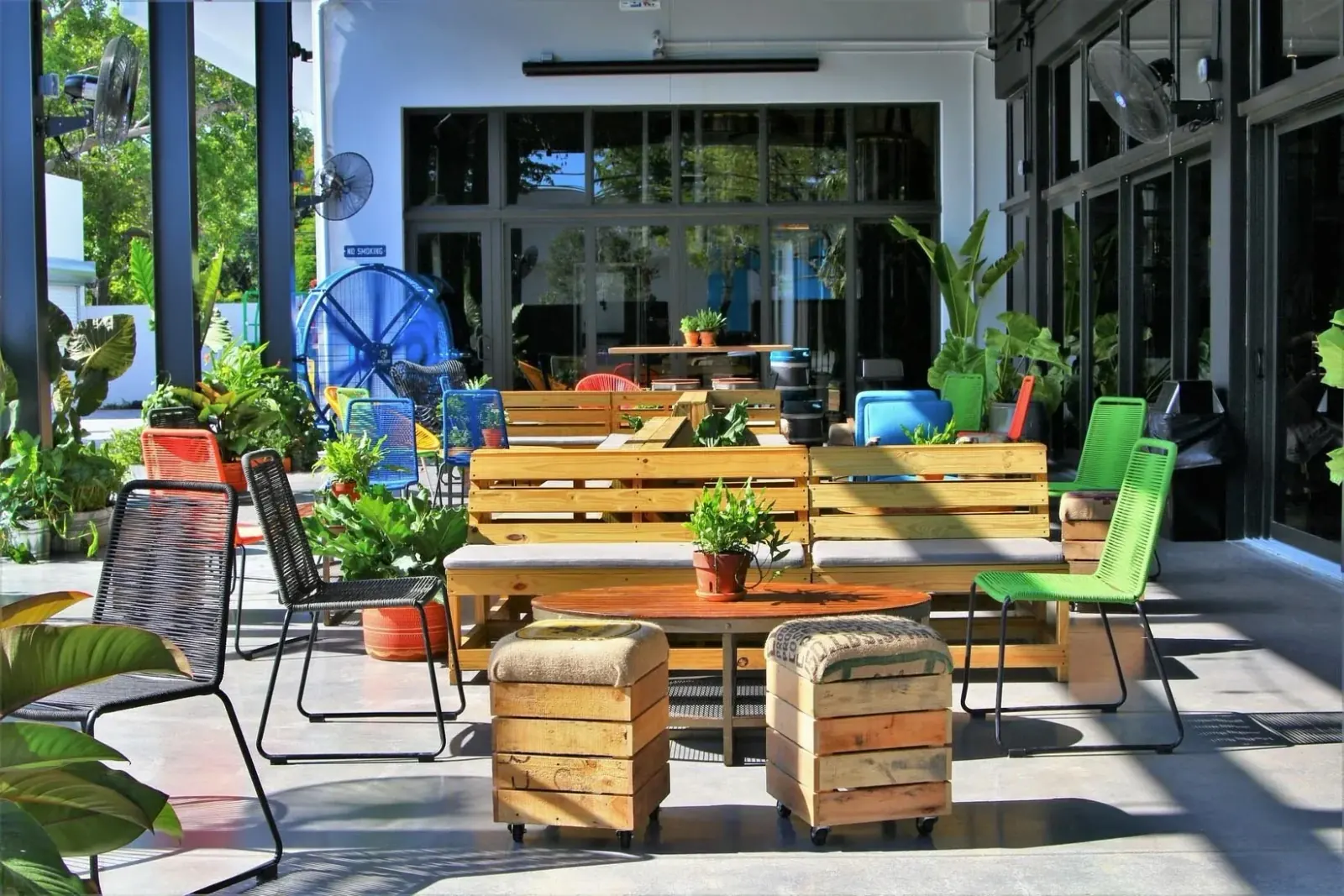 Outdoor covered patio with pallet-wood benches, colorful woven chairs and potted plants at Casa La Rubia, Miami