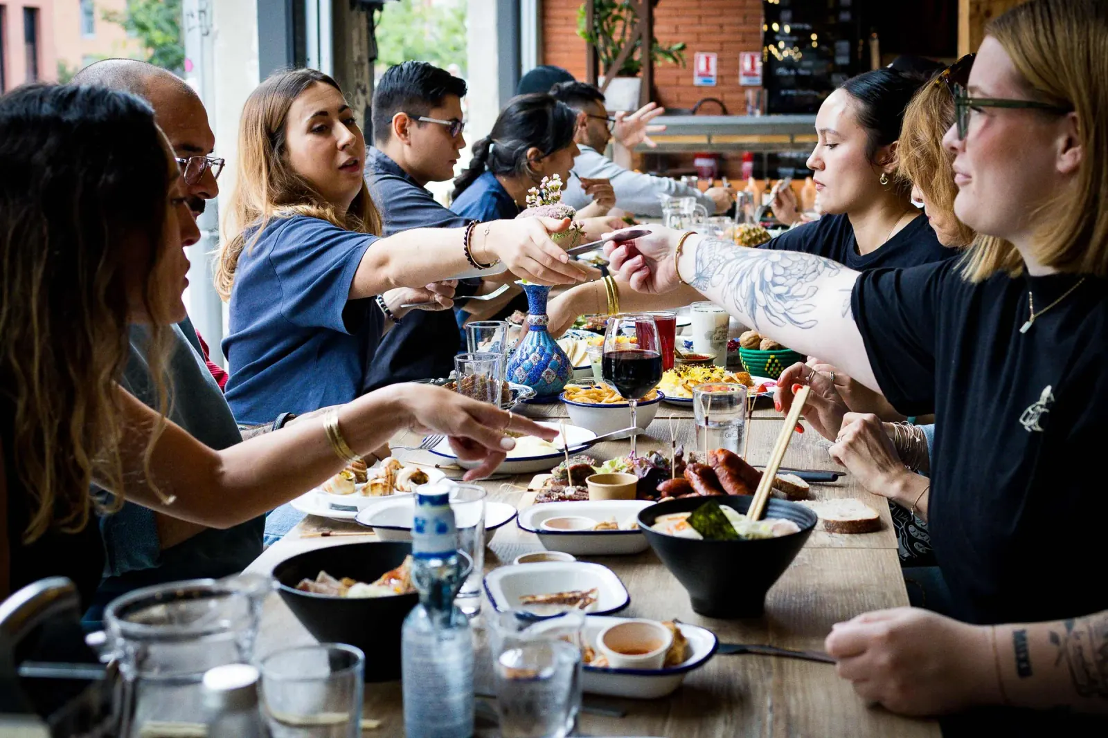 Guests sharing plates of food and drinks along a long communal wooden table inside the food hall at Les Halles de la Cartoucherie, Toulouse.