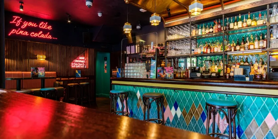 Curved bar counter, neon sign and teal tiled front inside Be At One in London