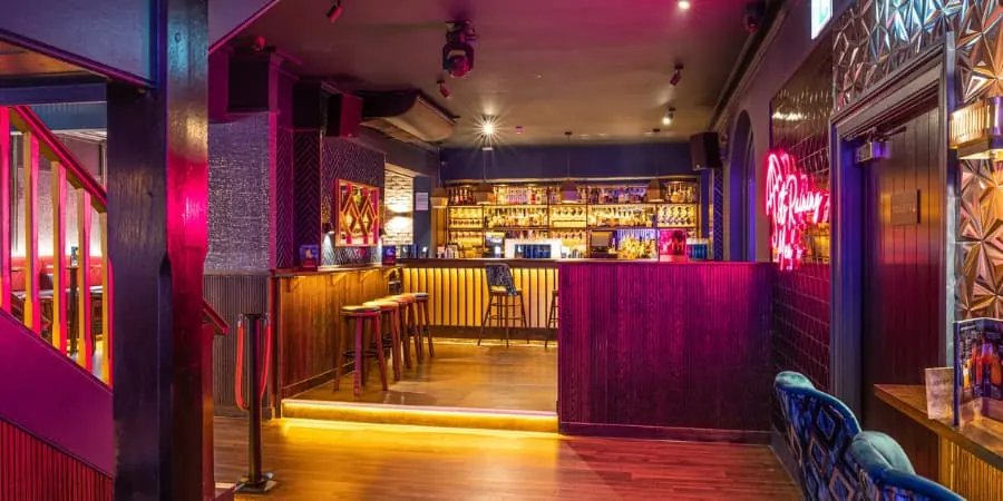 Pink and purple lit bar room with wooden floor and stools at Be At One in London
