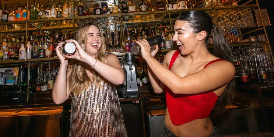 Two bartenders shaking cocktails in front of the backbar bottles at Be At One in London