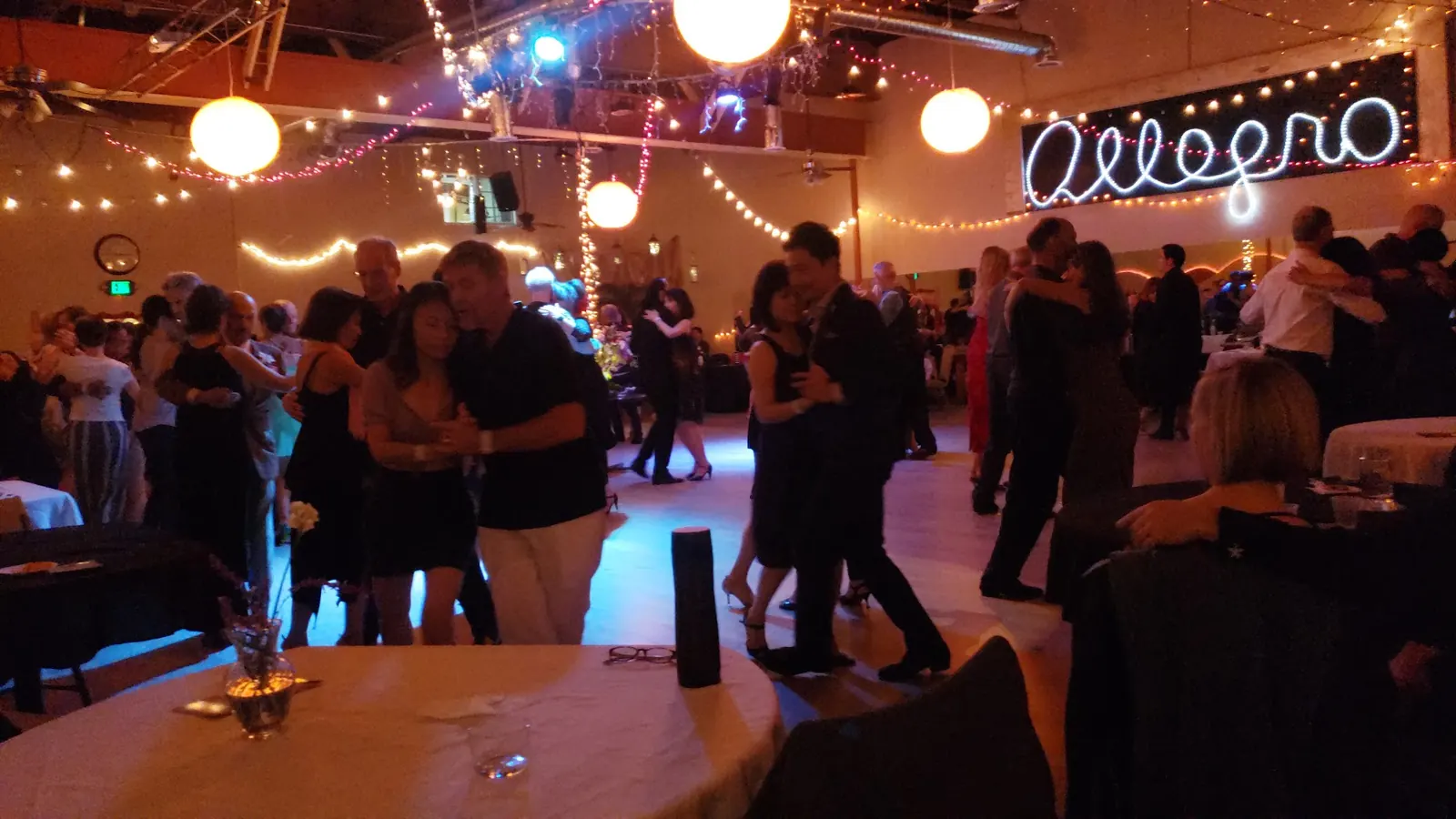 Busy social with many couples dancing under the Allegro sign and string lights