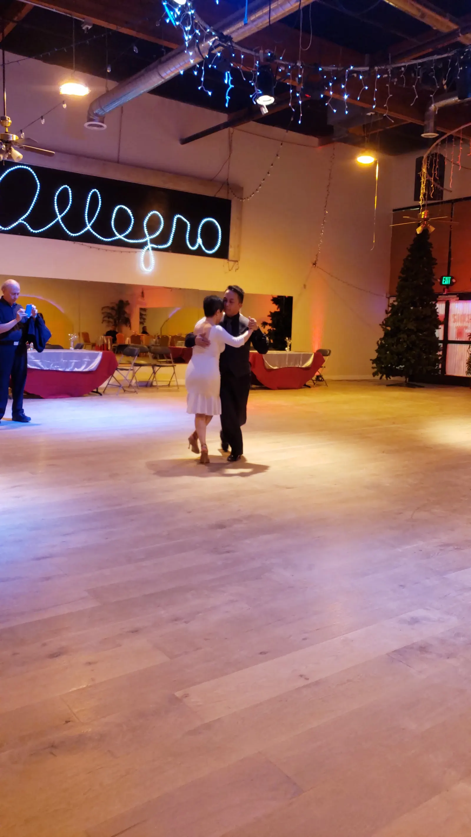 A couple dancing on the empty wooden floor below the Allegro neon sign