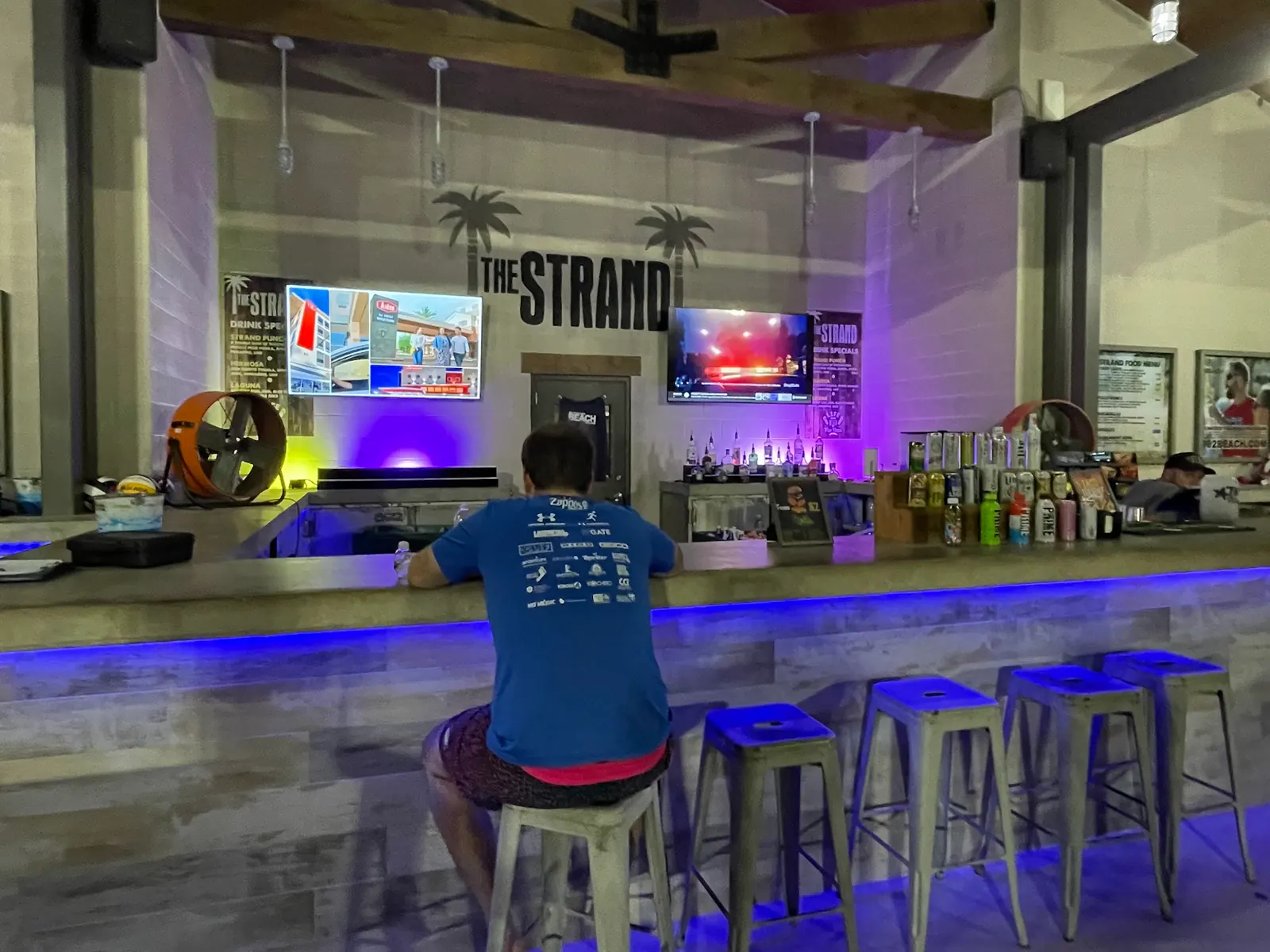 Indoor bar with blue lit counter and stools under The Strand lettering, Lewisville