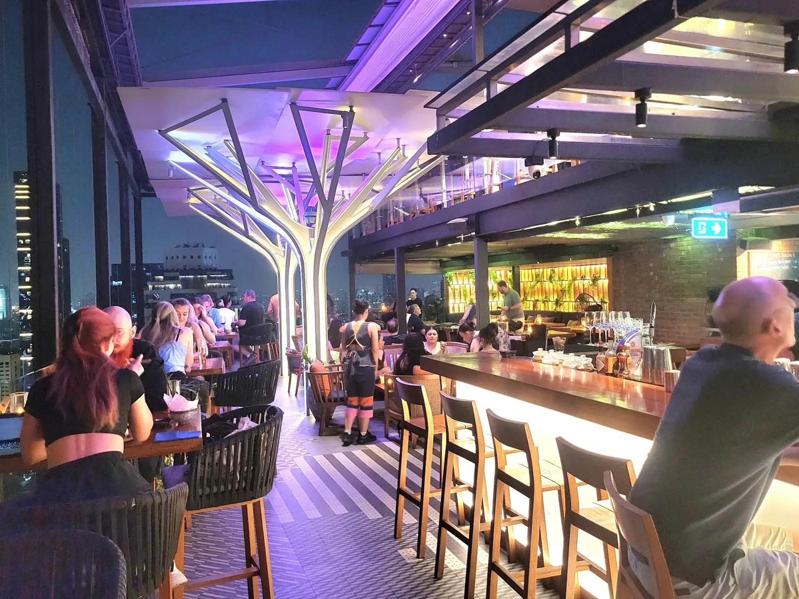 Bar interior with tree columns and guests at Above Eleven rooftop bar, Bangkok