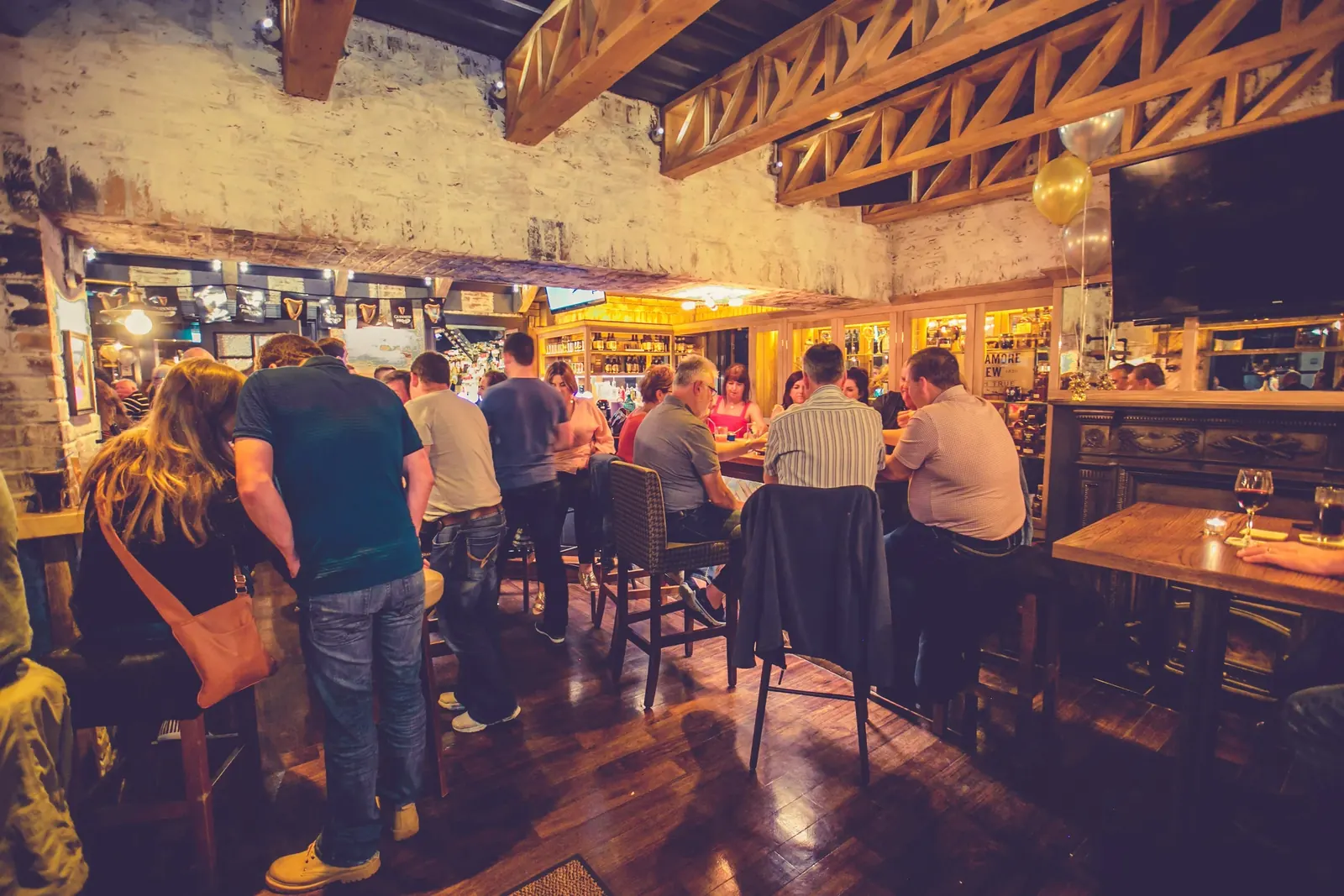 Guests at the bar under exposed wooden beams and whitewashed brick at Kennys of Lucan