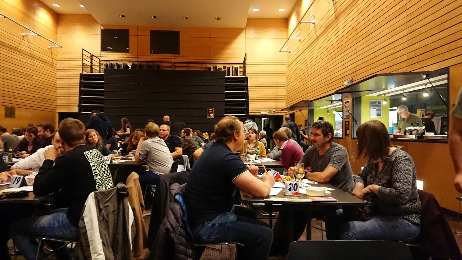 Guests at tables in the wood panelled hall at GC De Corren in Brussels with the bar hatch on the right
