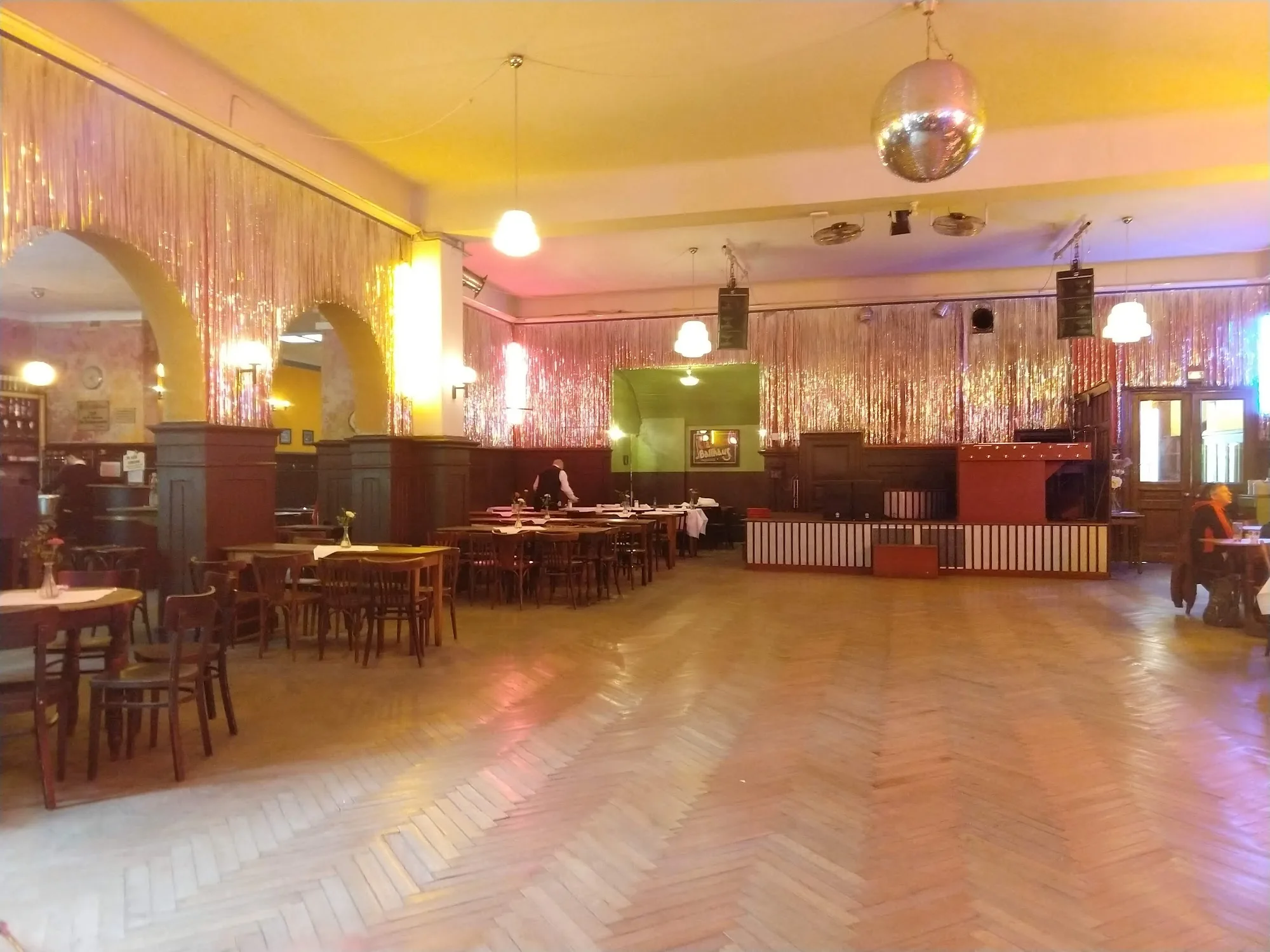 Historic ballroom with parquet dance floor, disco ball and gold tinsel curtains at Clärchens Ballhaus, Berlin