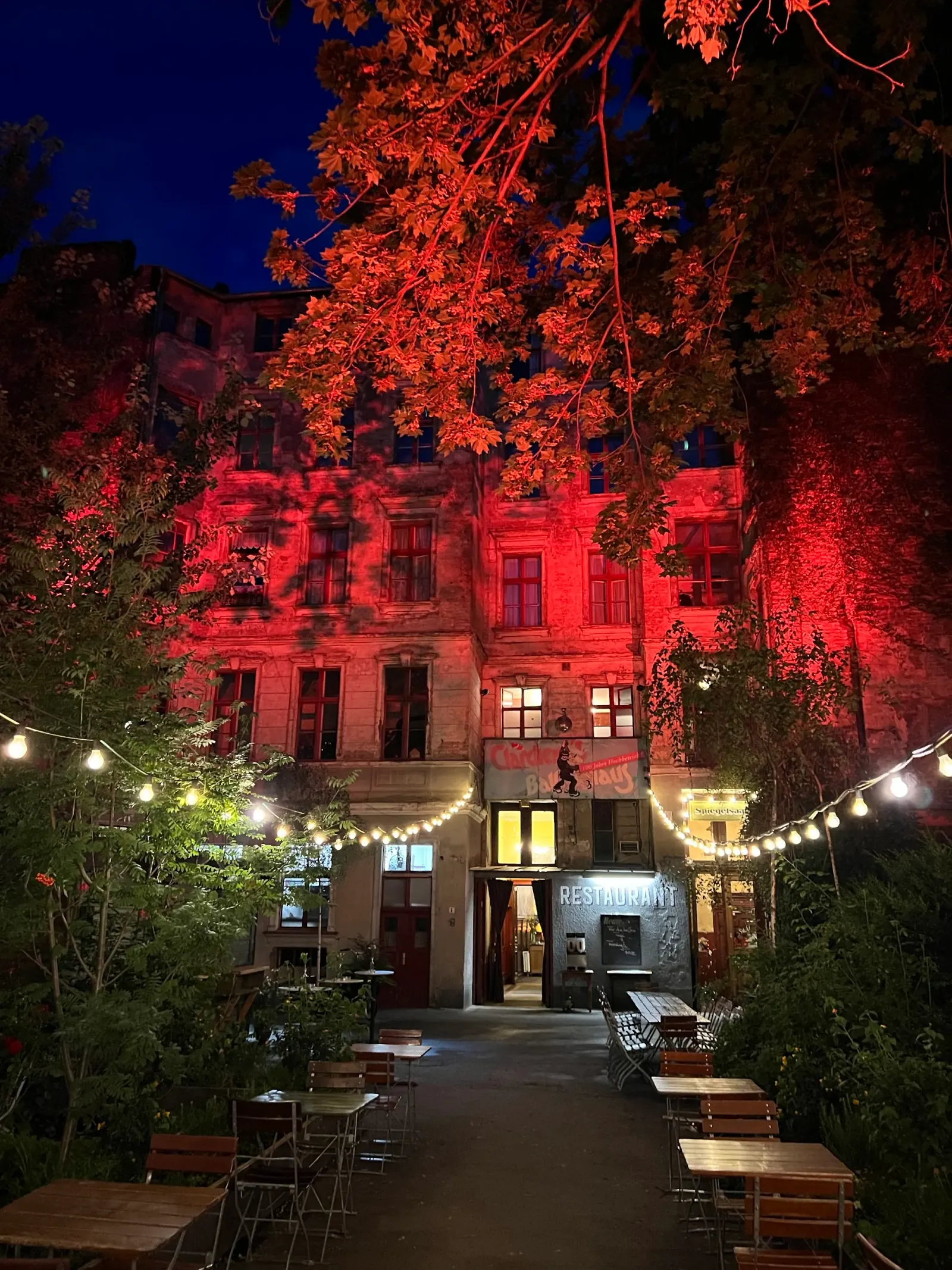 Red-lit night facade of Clärchens Ballhaus with illuminated signage and beer-garden tables, Berlin