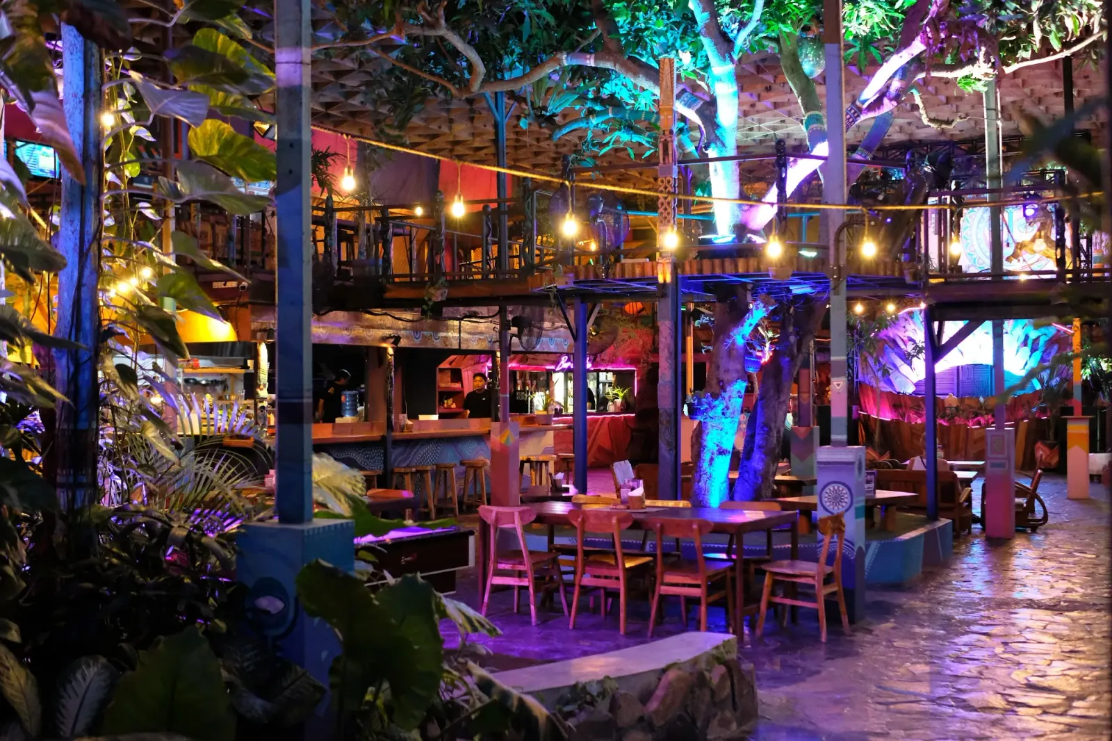 Colorful tropical interior with bar, lounge seating, and string lights at Hatch Bar in Bali