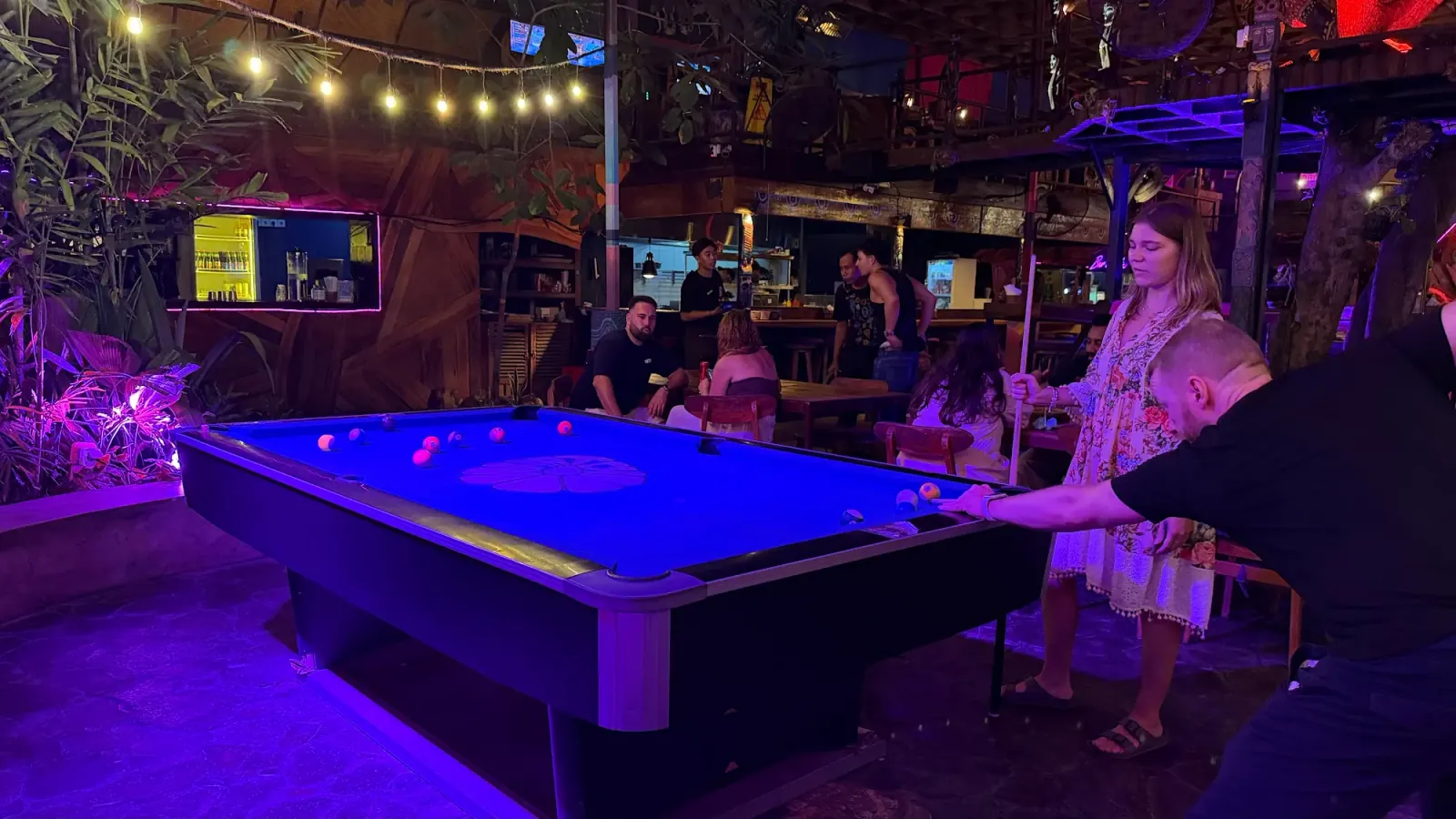 Guests playing pool under neon lights inside Hatch Bar in Bali