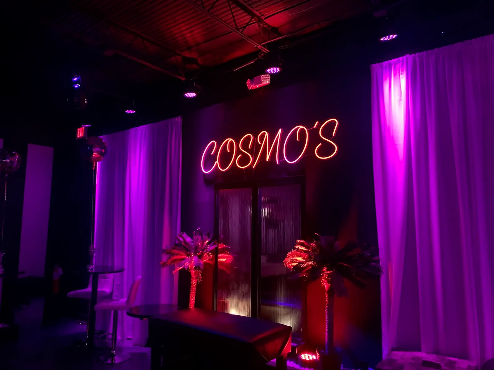 Red Cosmo's neon sign above lounge tables and drapes inside the nightclub