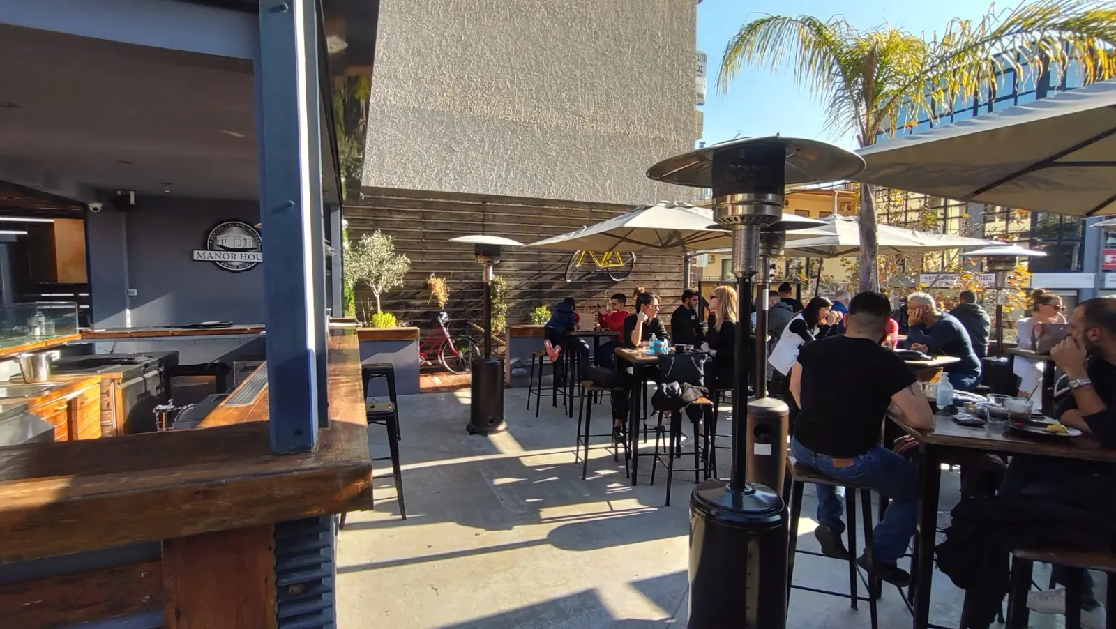 Manor House Athens sunny outdoor patio with guests and Manor House signage in background