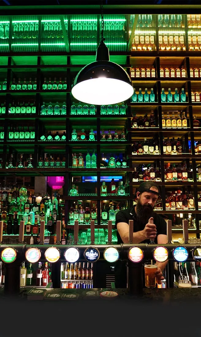Distinctive green-lit bar interior with bottle wall and bartender at O'Sullivans Paris, home of SalsaO'Sulli