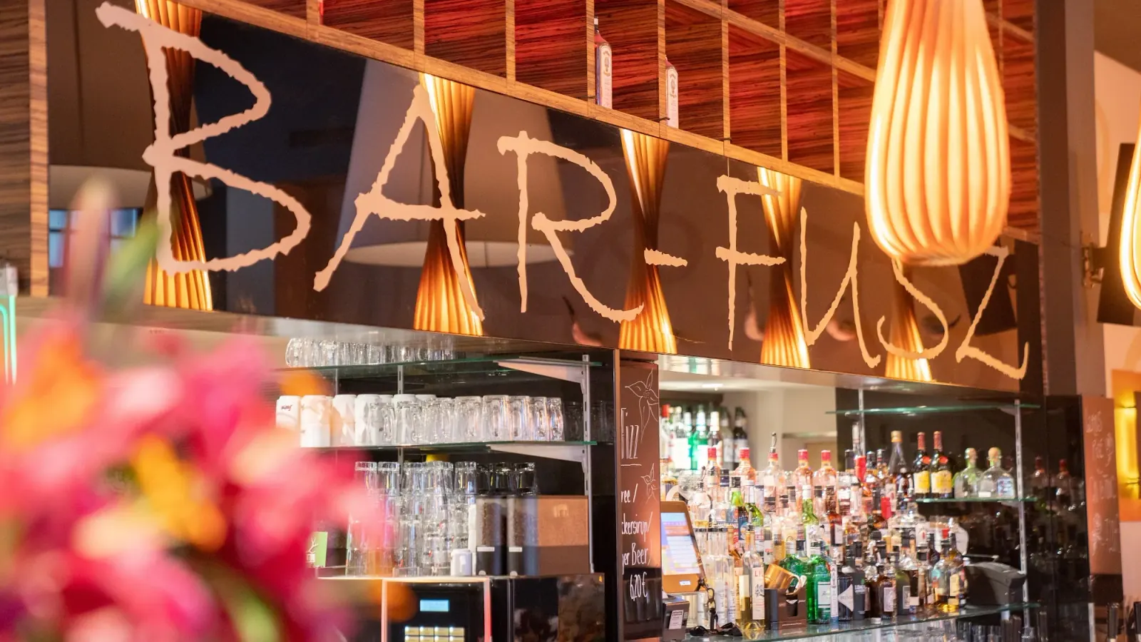 Bar counter with BAR-FUSZ branded sign and warm orange lighting at Barfusz Leipzig