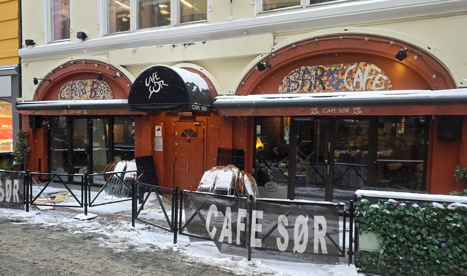 Snow-covered street exterior of Cafe Sor with CAFE SOR signage in Oslo