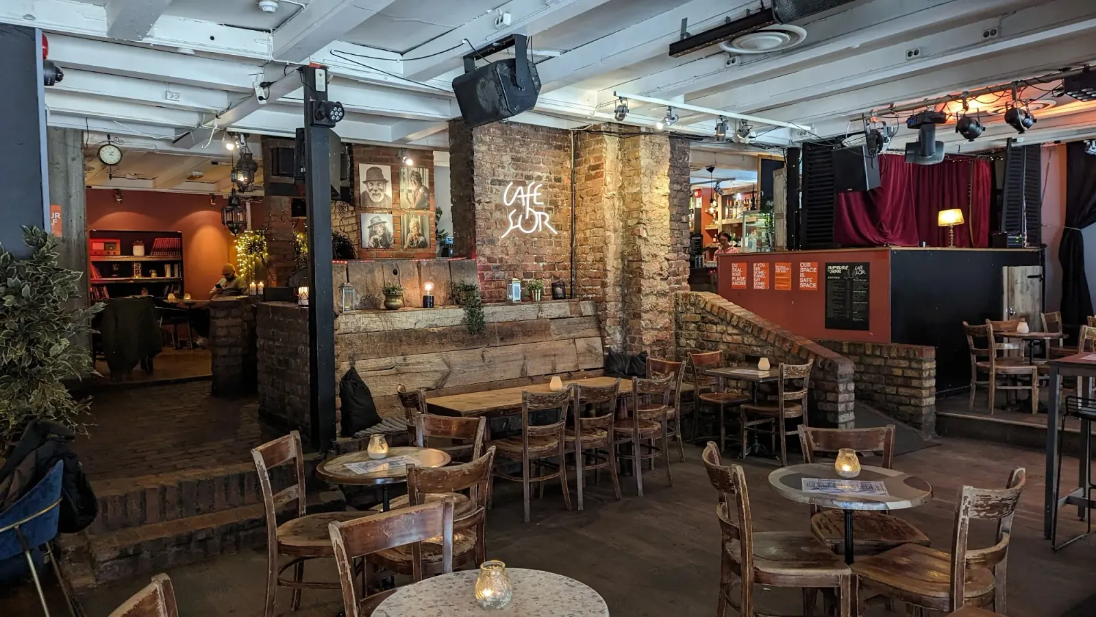 Interior of Cafe Sor with brick stage backdrop, bar and clustered tables