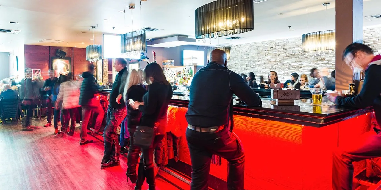 Busy bar and lounge interior at Smokeshow BBQ and Brew Toronto with people gathered along the counter under red accent lighting