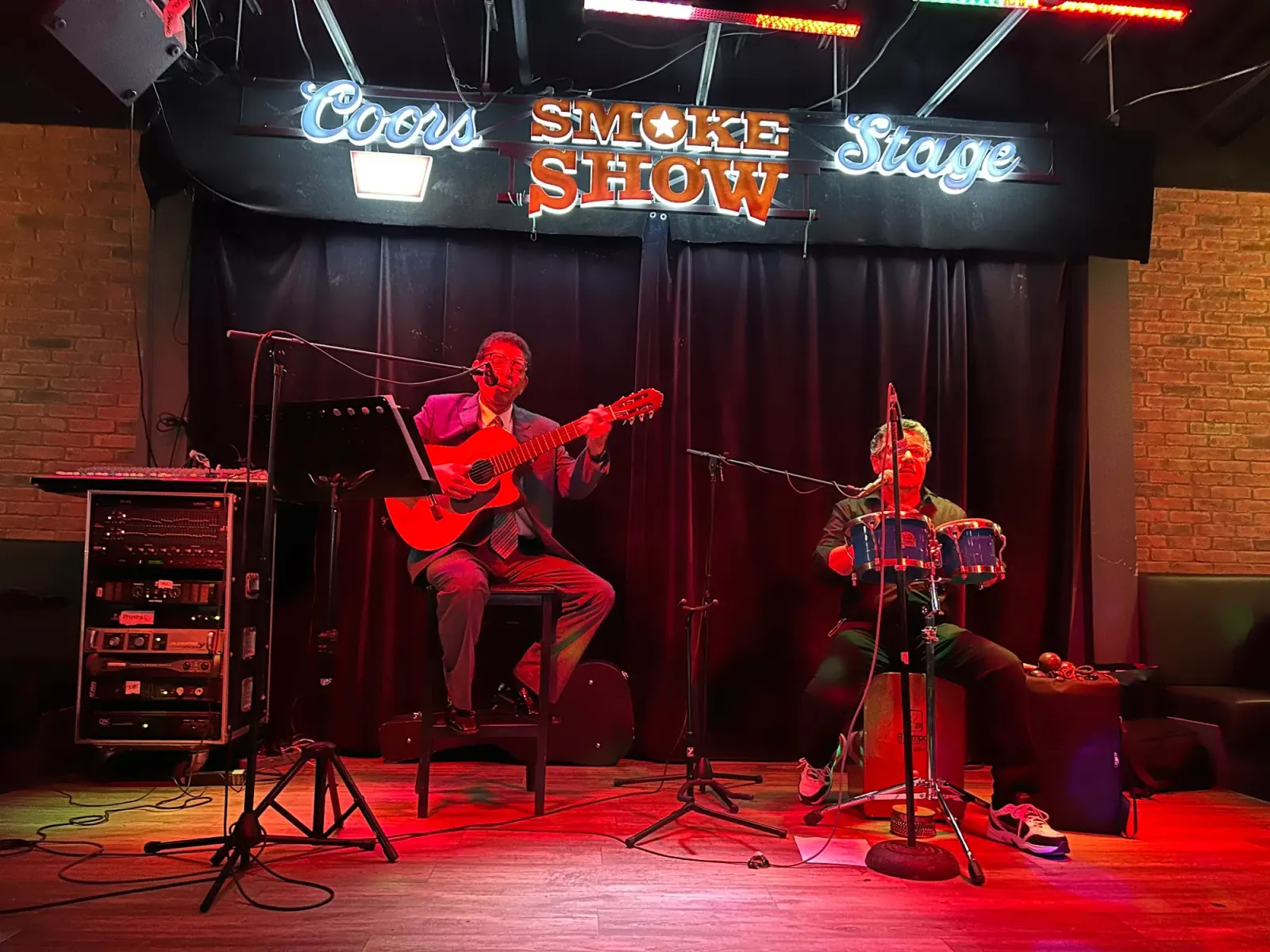 Two musicians performing on the neon-lit Smoke Show stage inside Smokeshow BBQ and Brew Toronto