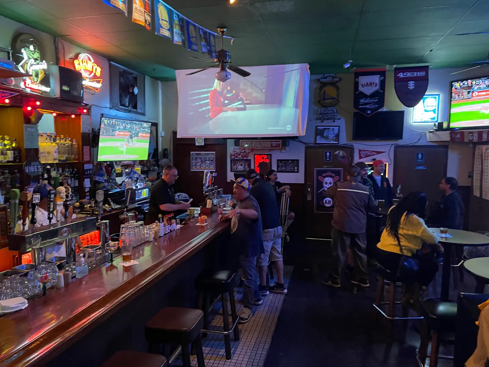 Long bar with stools and guests inside Il Pirata in San Francisco under screens and neon signs