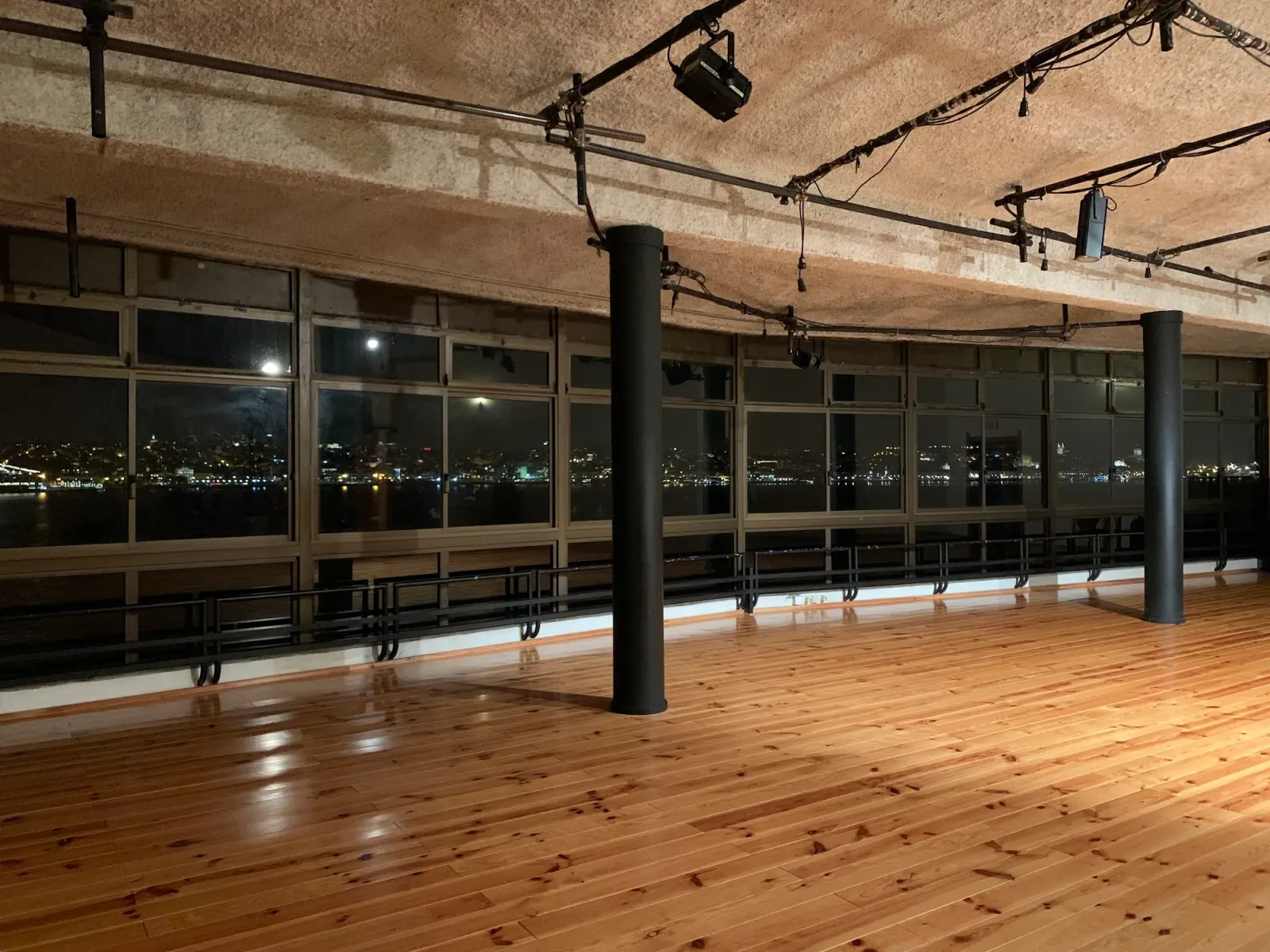Wooden dance floor with stage lighting and Lisbon skyline view at Ponto de Encontro, Almada
