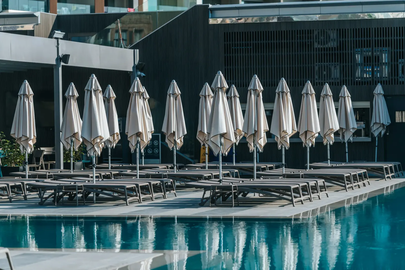 Poolside deck with rows of grey sun loungers and closed parasols beside the pool at Aqualuna Beach Club, Malta