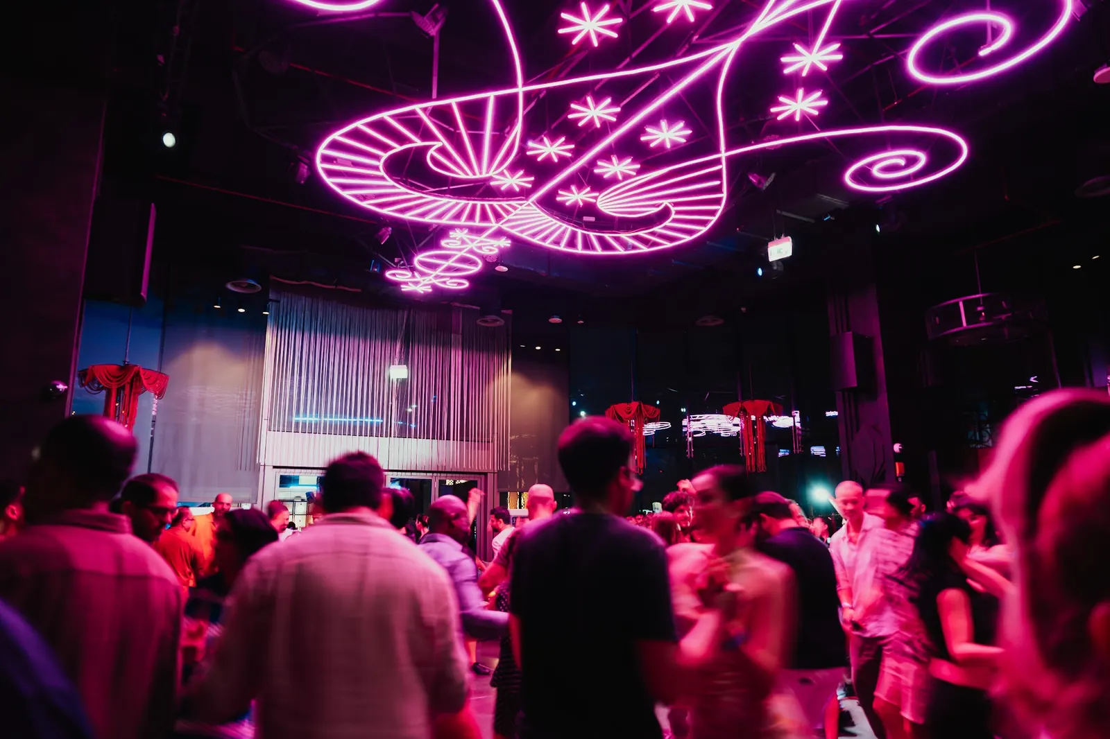 A packed crowd under the pink neon ceiling artwork at SoBe Rooftop Bar in Dubai
