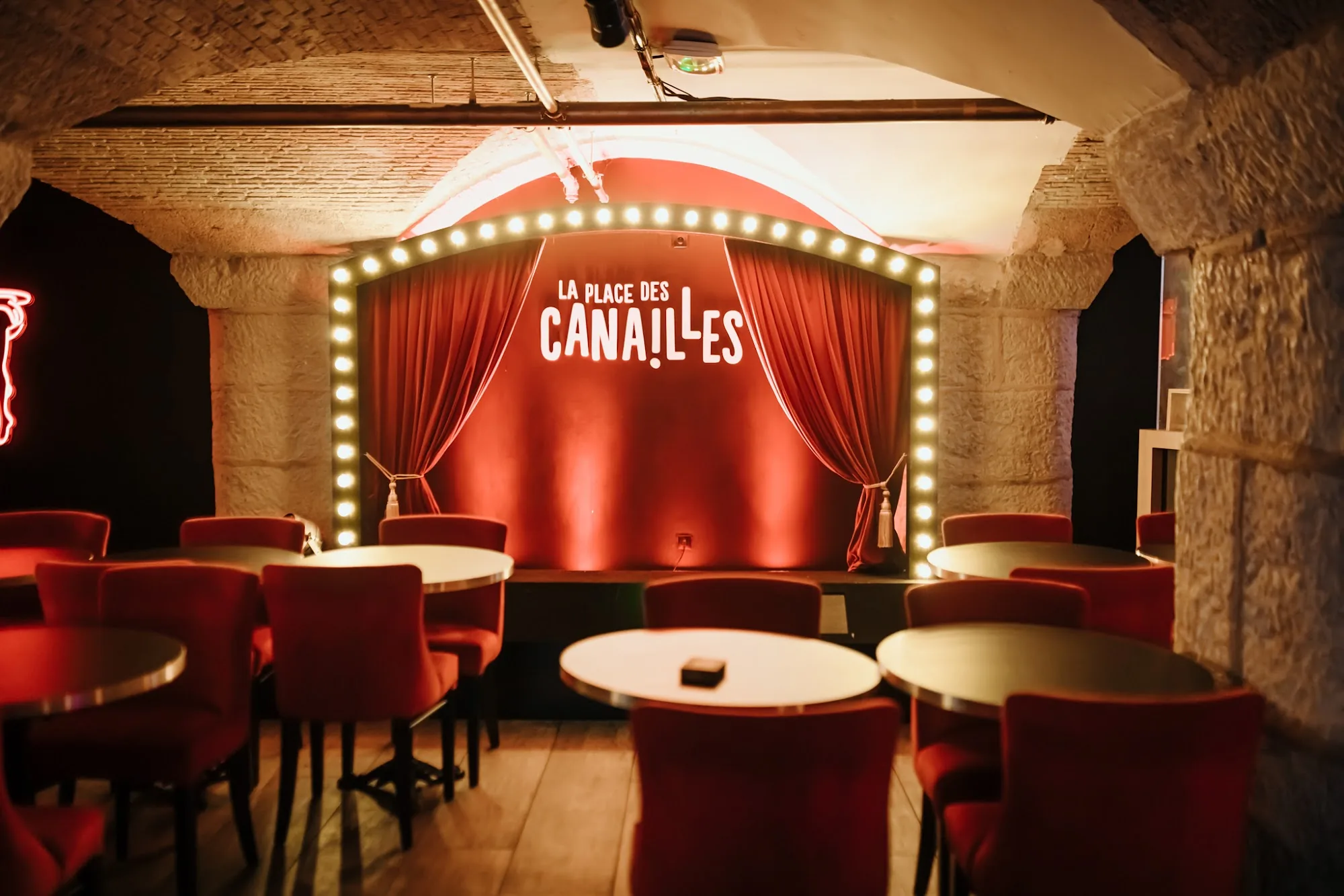 Stage with La Place des Canailles illuminated marquee sign, empty seating area in front
