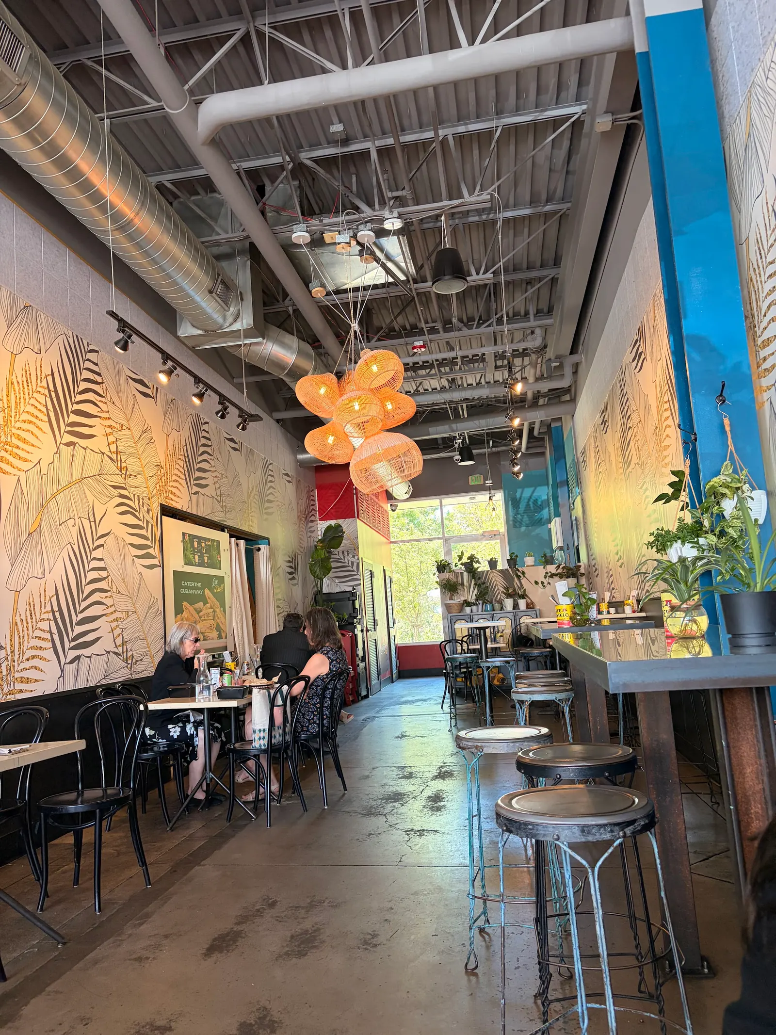 Bar stools, bistro tables and leaf mural inside Cuba Cuba Sandwicheria, Denver