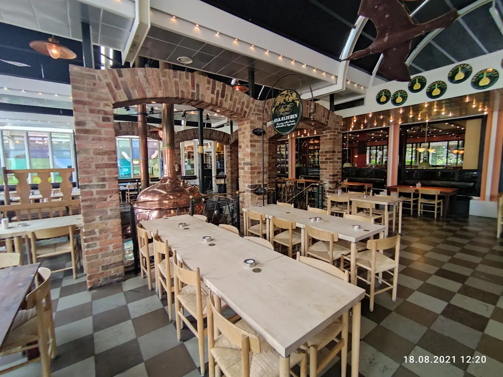 Interior of The Old Irish Pub Copenhagen with brick archways, a copper brewing kettle and string lights over wooden tables
