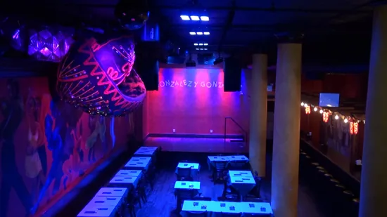 Interior of Gonzalez y Gonzalez dance venue in New York showing the dance floor, stage, and colorful Latin murals under neon lights