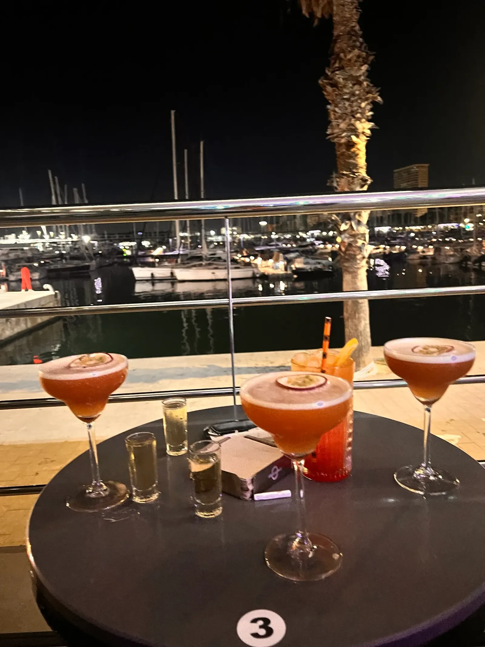 Cocktails on a William Buzz table overlooking the lit-up Alicante marina at night