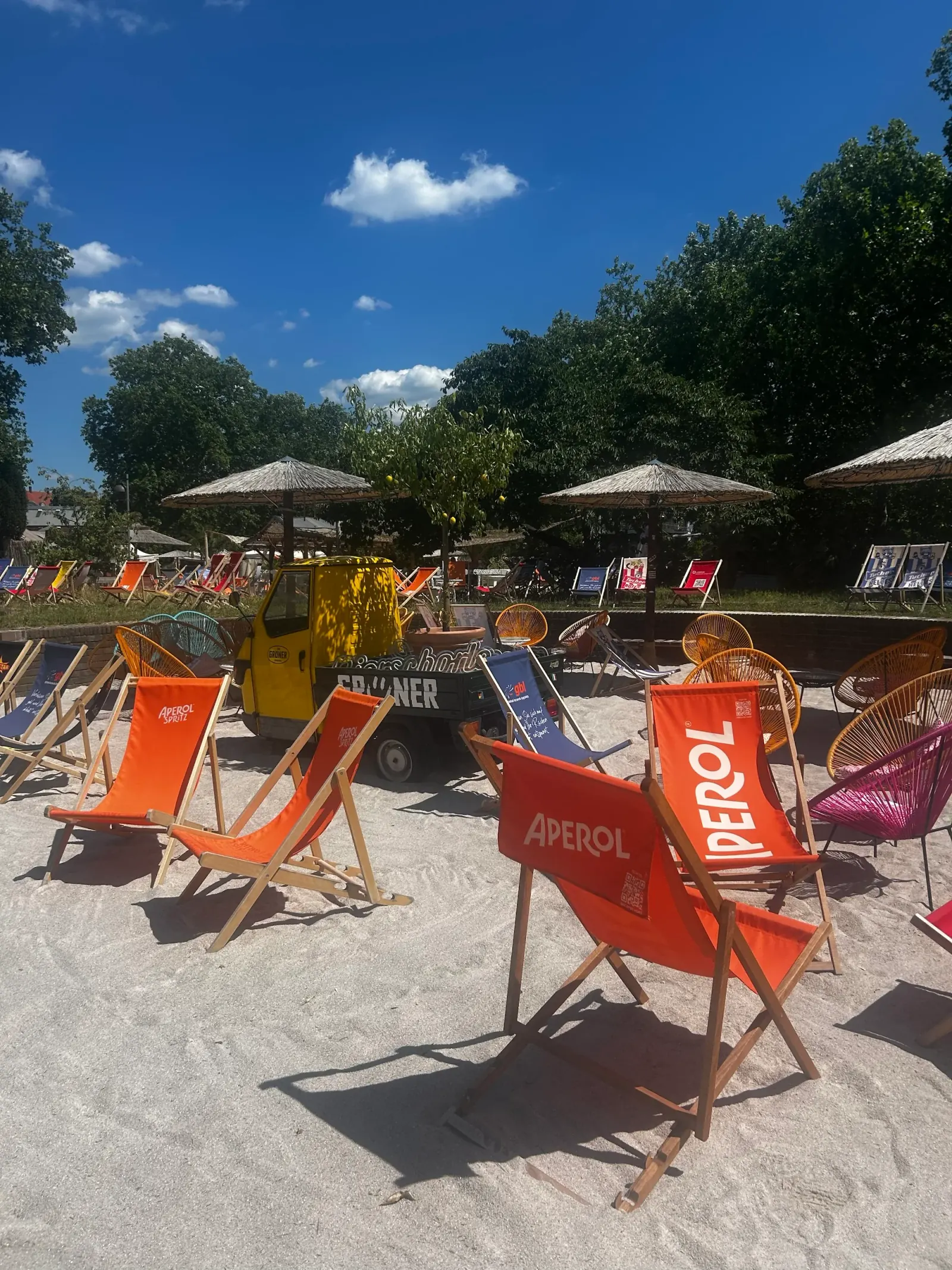 Colorful Aperol-branded deckchairs on sandy beach at Lieblingsstrand with parasols and a tuk-tuk bar