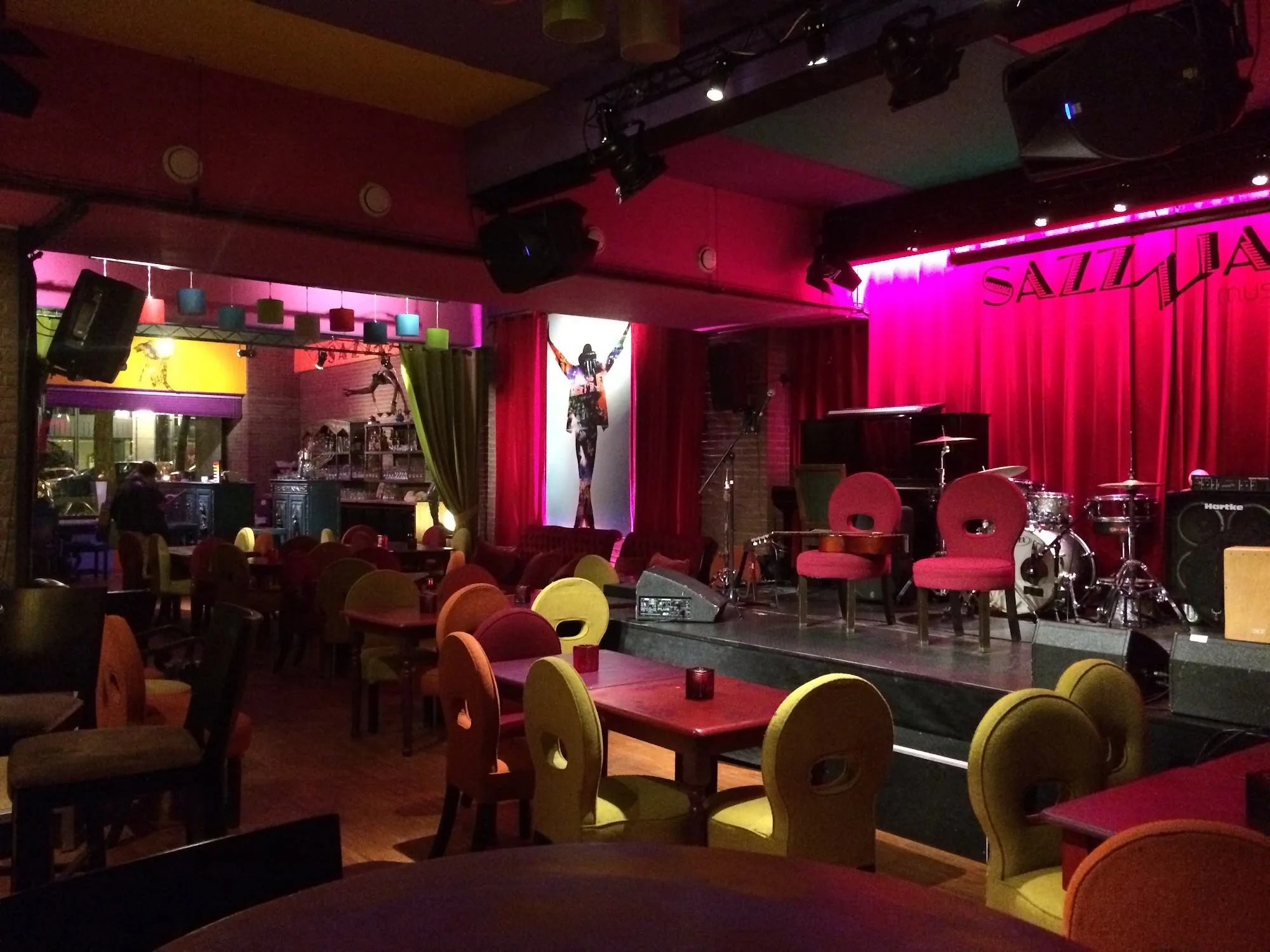 Pink-lit stage with drum kit and colorful seating in the main music room at The Embassy Room Brussels