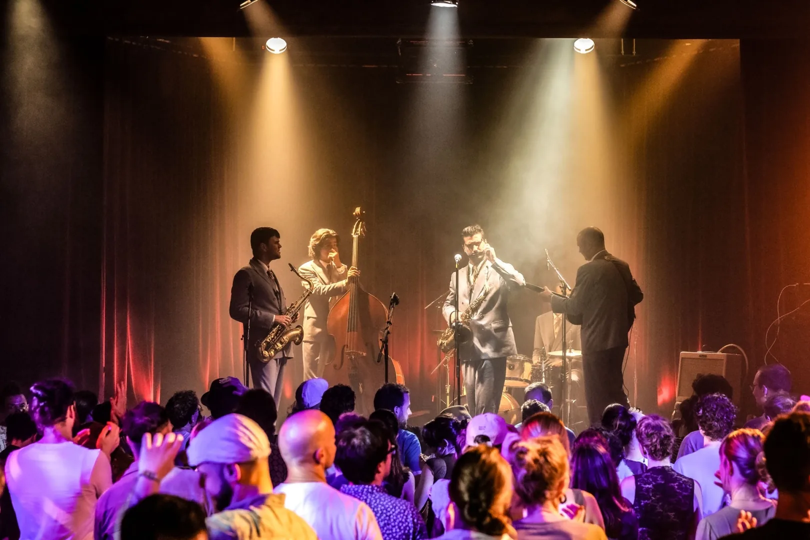 Live band performing on stage under warm spotlights at Albert Hall Brussels while a packed crowd dances and cheers below
