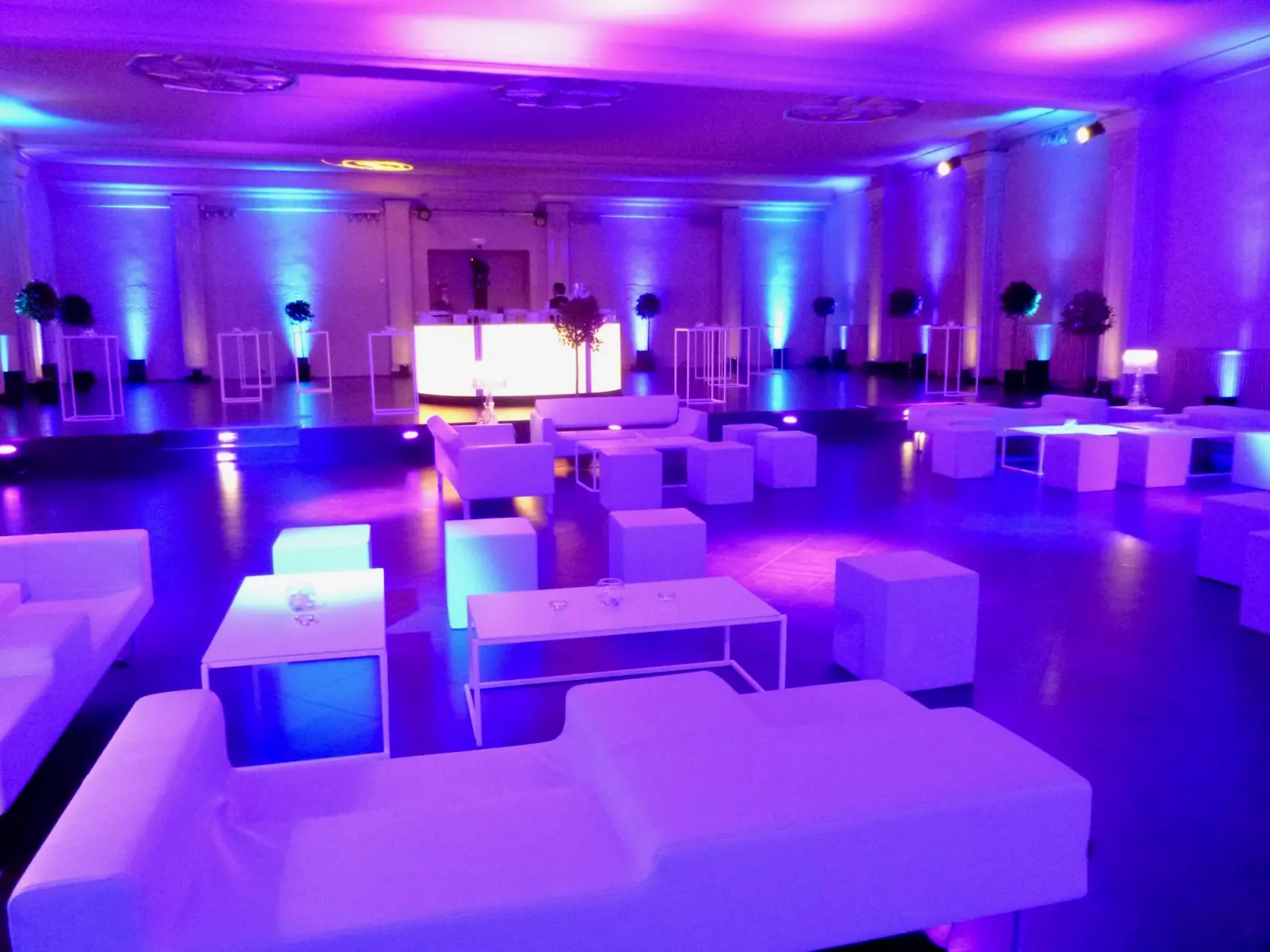 Purple and blue club lighting over white lounge seating and a lit bar in the main hall of Albert Hall Brussels set up for a party